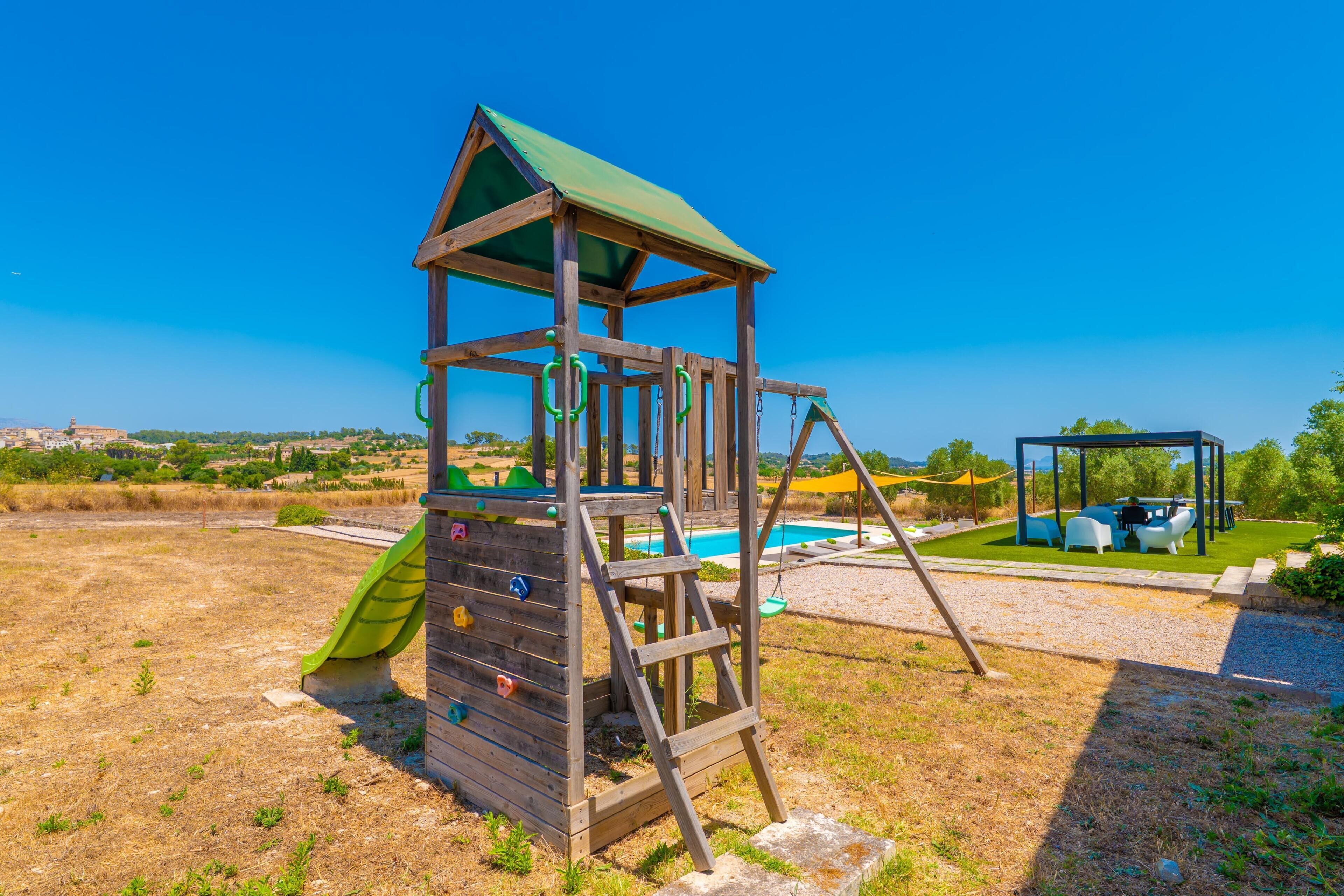 A wooden play structure with a slide and climbing holds, a swing set, and a pool area with outdoor seating.