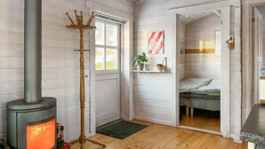 A cozy room with a wood-burning stove, a coat rack, a bed, and a shelf with a plant. - Beautiful home in Vordingborg with WiFi (Vordingborg)