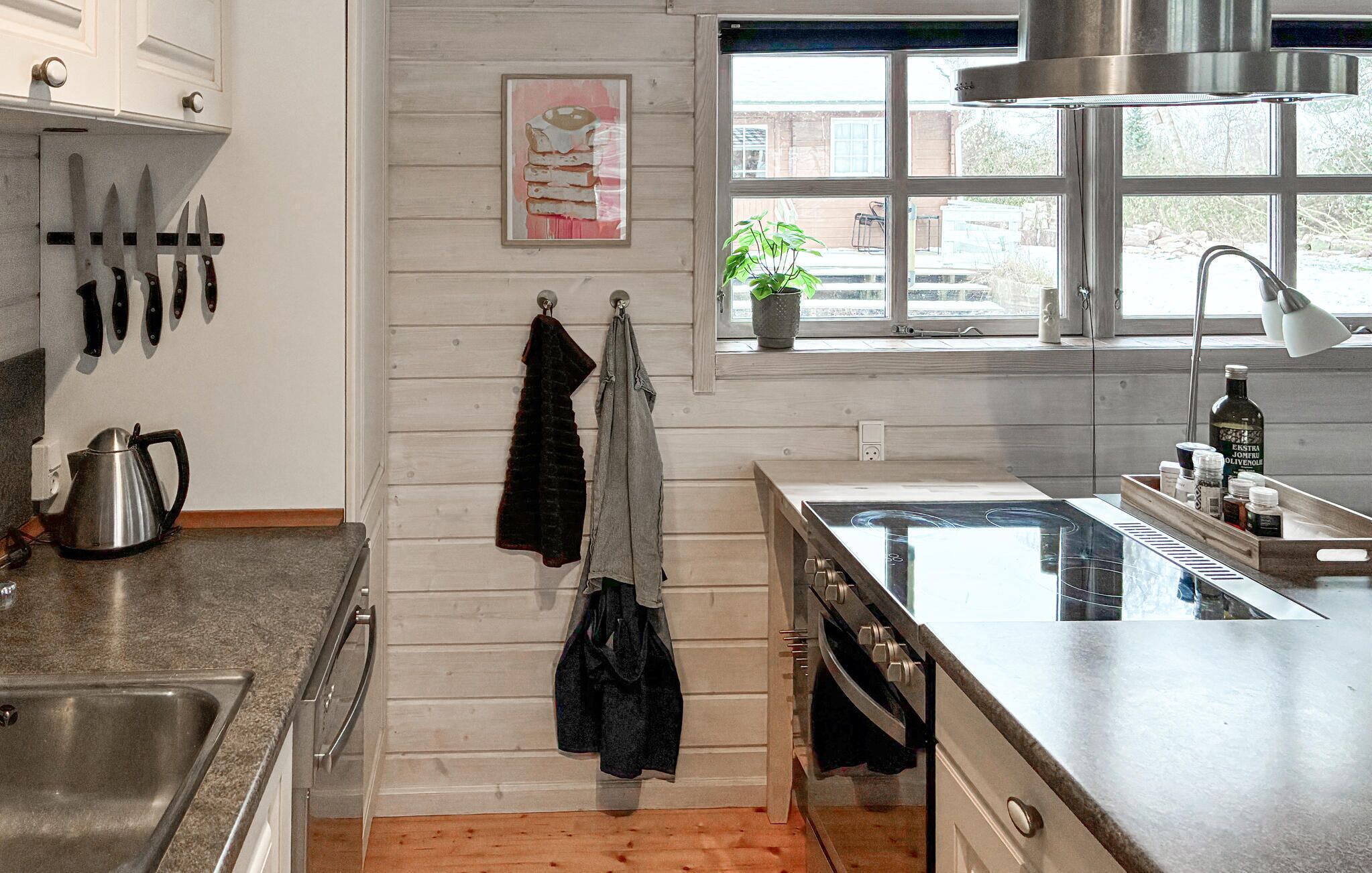 A kitchen with wooden walls, a window with a view, a sink, and a stove.