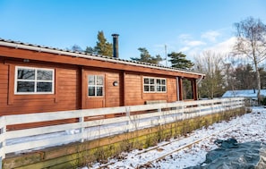A wooden cabin with a white porch, a chimney, and a fenced area with snow. - Beautiful home in Vordingborg with WiFi (Vordingborg)