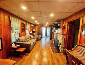 A cozy cabin interior with a wooden floor, a stone fireplace, a sofa, and a television.