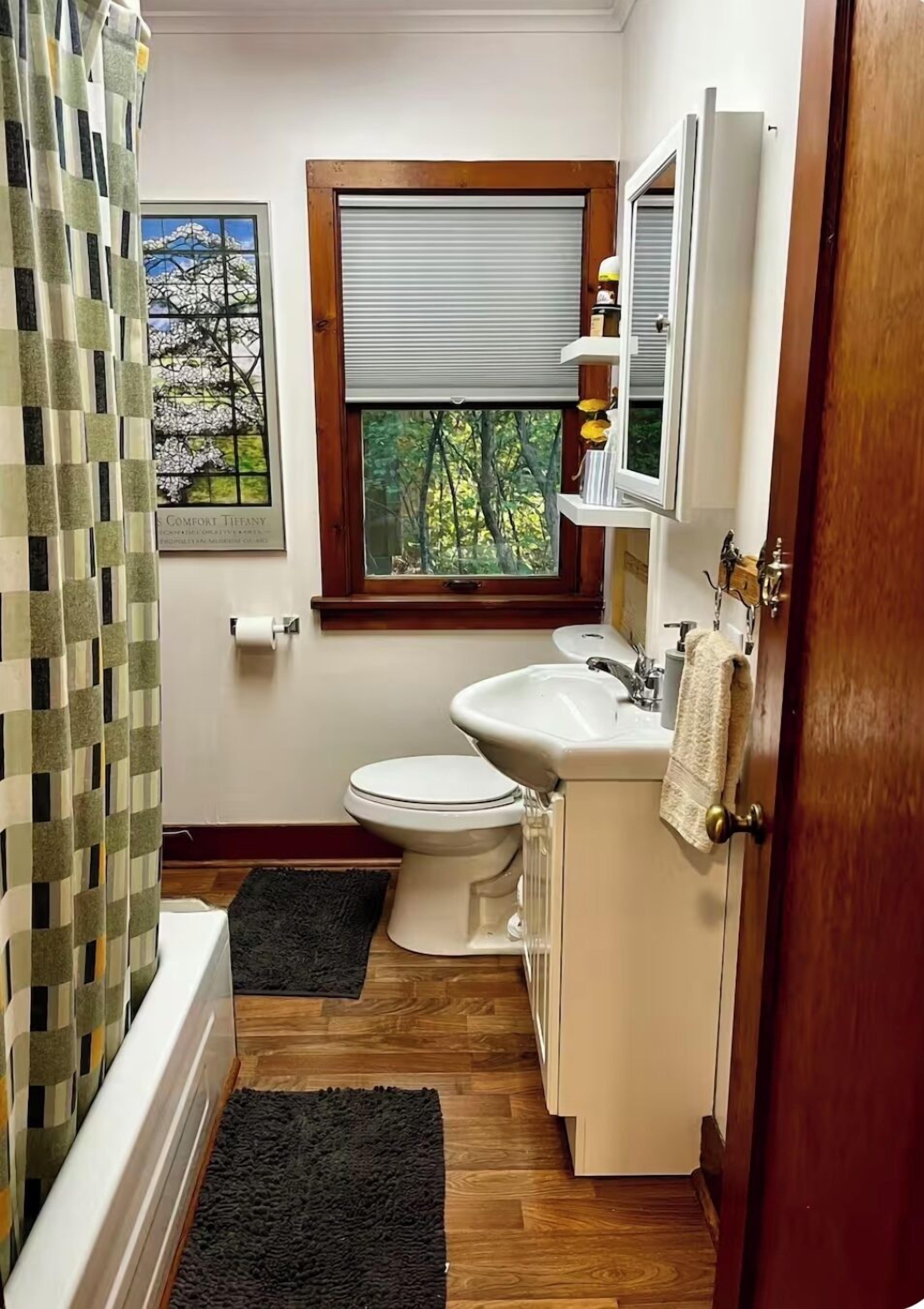 A bathroom with a toilet, sink, and window. There is a towel rack and a shower curtain.