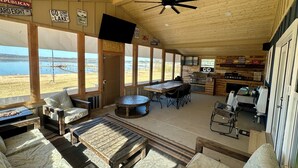 A rustic cabin with a large dining table, comfortable seating, a kitchen area, and a view of the lake. - Lakefront Home with Private Beach & Dock, Great Sunsets, 7 Miles from Rocker B (Graford)