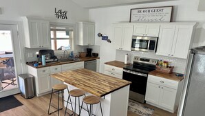 A modern kitchen with white cabinets, a wooden island with stools, stainless steel appliances, and a sign that reads "BE OUR GUEST". - Lakefront Home with Private Beach & Dock, Great Sunsets, 7 Miles from Rocker B (Graford)