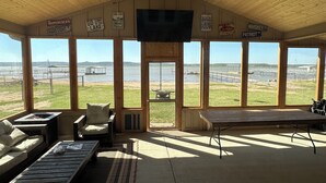 A room with large windows, a ceiling fan, and a television. - Lakefront Home with Private Beach & Dock, Great Sunsets, 7 Miles from Rocker B (Graford)