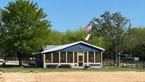 A building with a blue roof and a flagpole, located near a body of water. - Lakefront Home with Private Beach & Dock, Great Sunsets, 7 Miles from Rocker B (Graford)