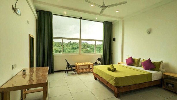 A bedroom with a bed, a desk, a chair, and a window with a view of greenery. - Kandy Hotel Riverline Resort (Kandy)