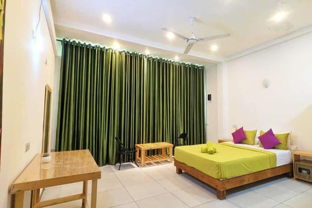 A bedroom with a bed, a desk, a chair, a ceiling fan, and a window with curtains.