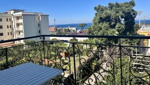 Ein Balkon mit Blick auf das Meer, einen Baum und Gebäude im Hintergrund.