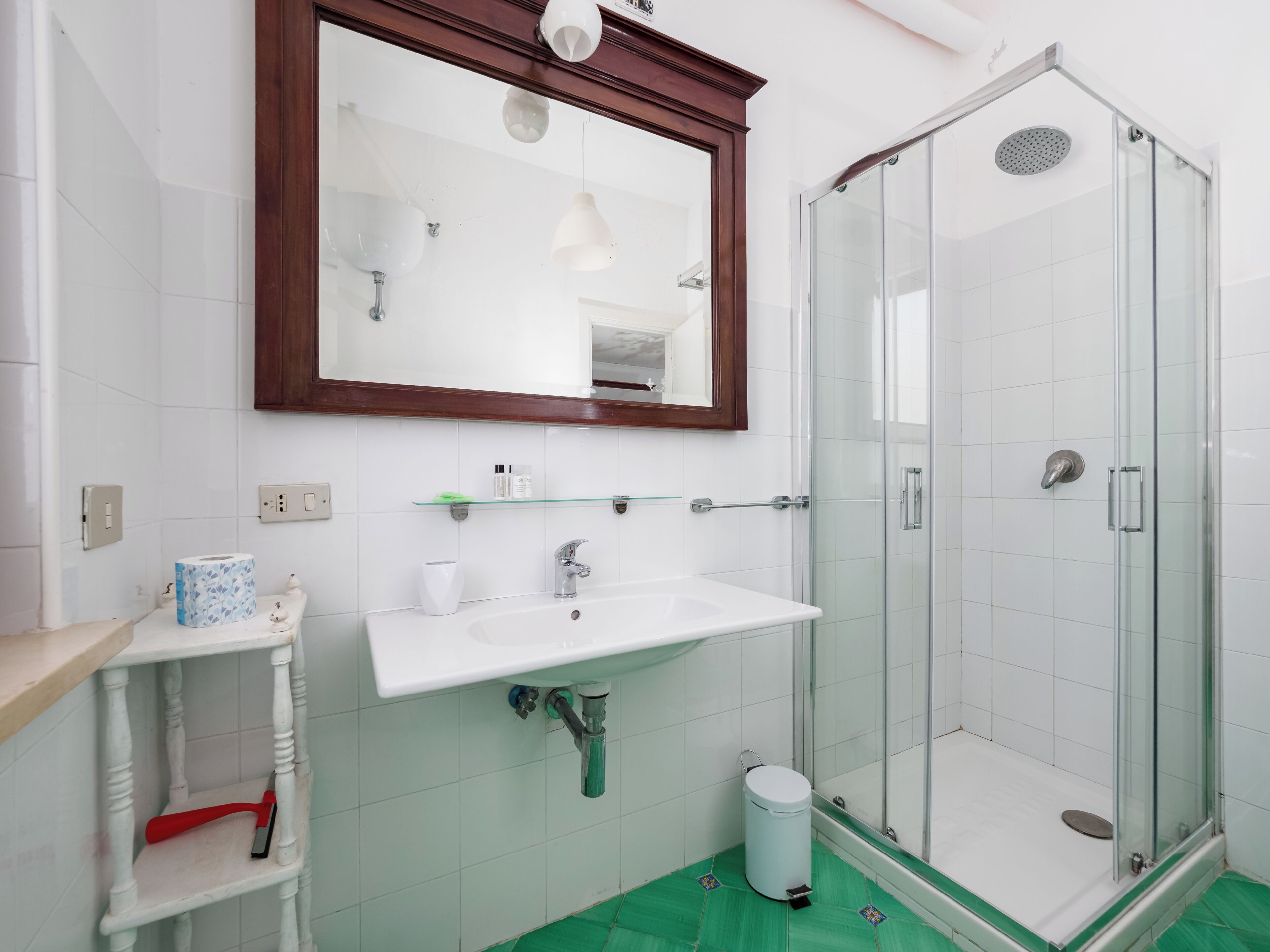 A bathroom with a white sink, a mirror, a glass shower enclosure, and a green floor.