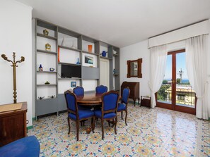 A dining area with a table and chairs, a television on a shelf, and a view through a window. - Casa Sofia (Sorrento)