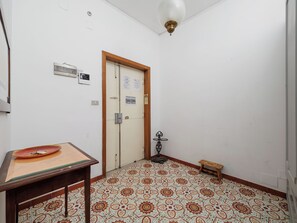 A room with a patterned floor, a door with a wooden frame, a small table with a plate, and a wall-mounted light fixture. - Casa Sofia (Sorrento)