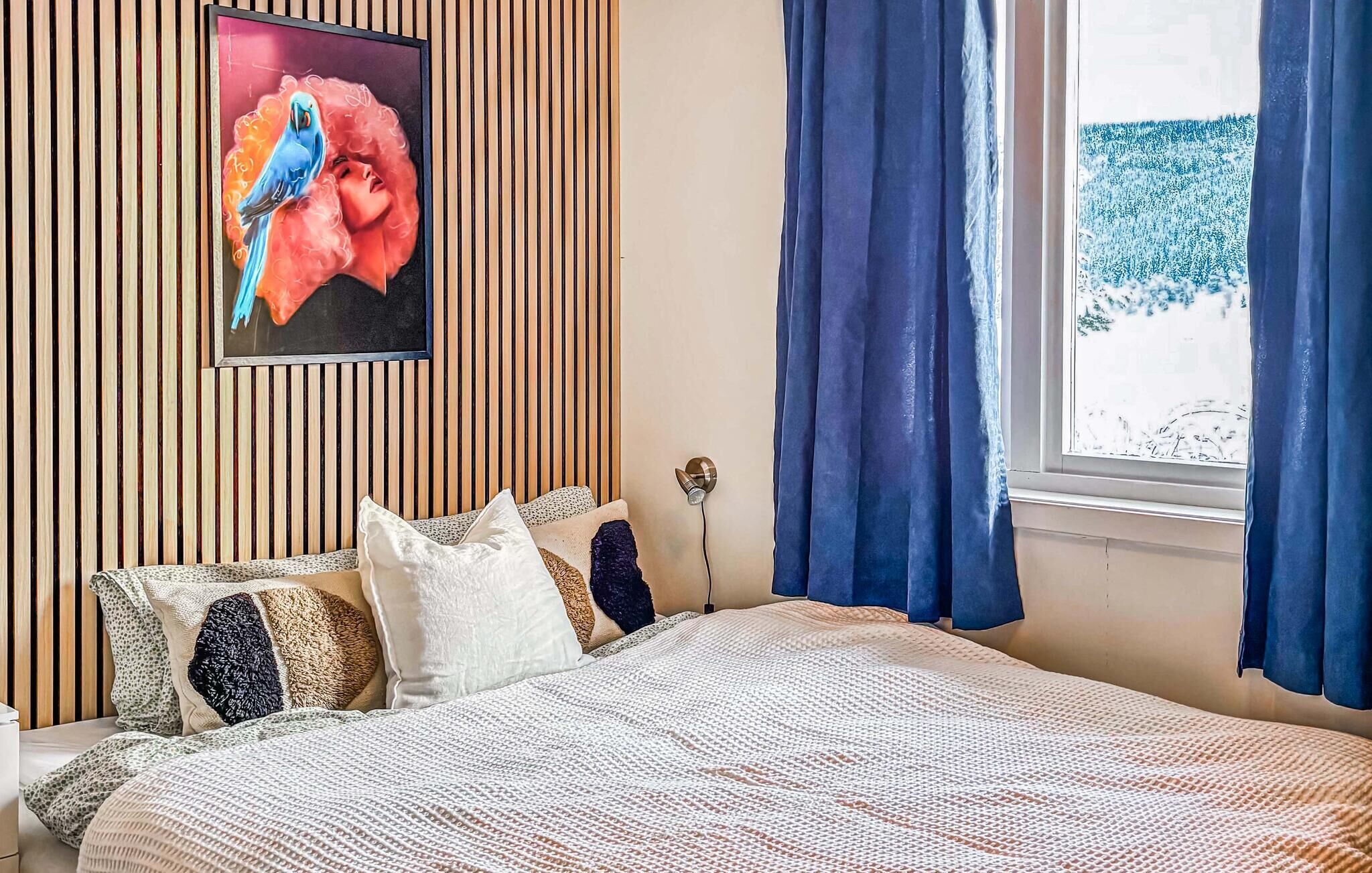 Ein Schlafzimmer mit einem Bett, Kissen, einem Wandbild und einem Fenster mit Vorhängen.