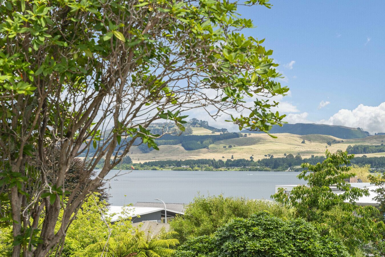 A lakeside view with a building in the foreground, surrounded by greenery and hills in the background.