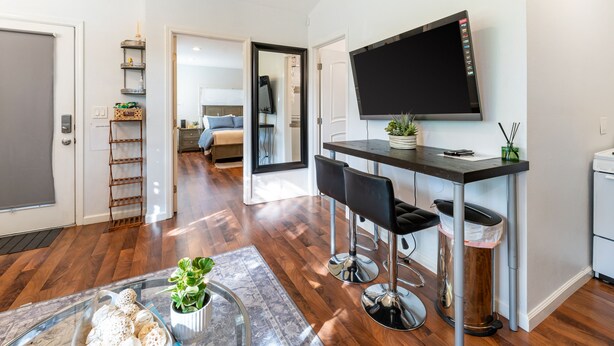 A modern kitchen with a flat-screen TV, bar stools, and a potted plant.