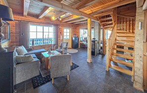 Ein Holzblockhaus-Innenraum mit Wohnbereich, der eine Couch, Sessel, einen Couchtisch und einen Kamin zeigt.