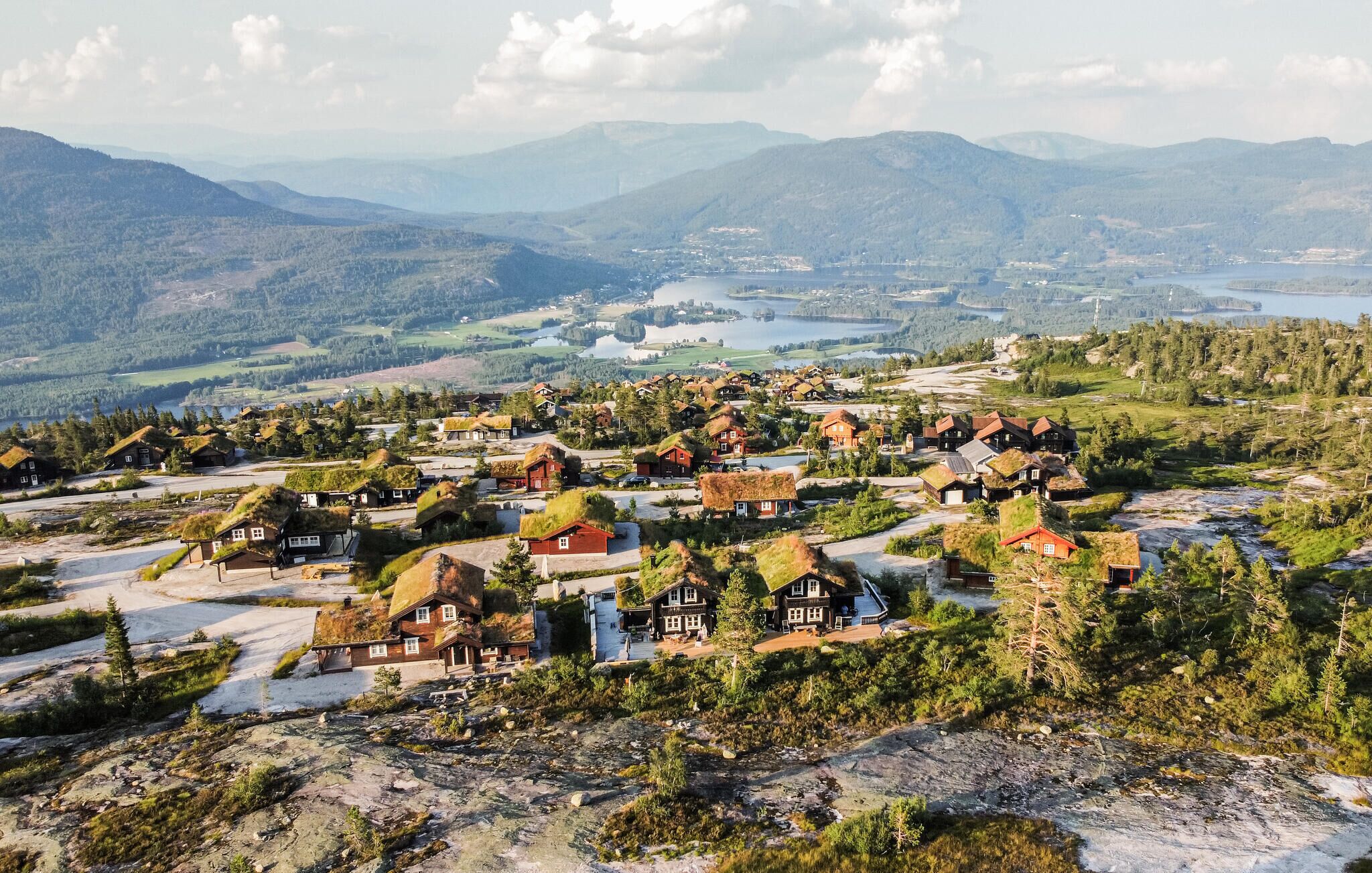 A village with traditional houses featuring thatched roofs, surrounded by mountains and a lake.