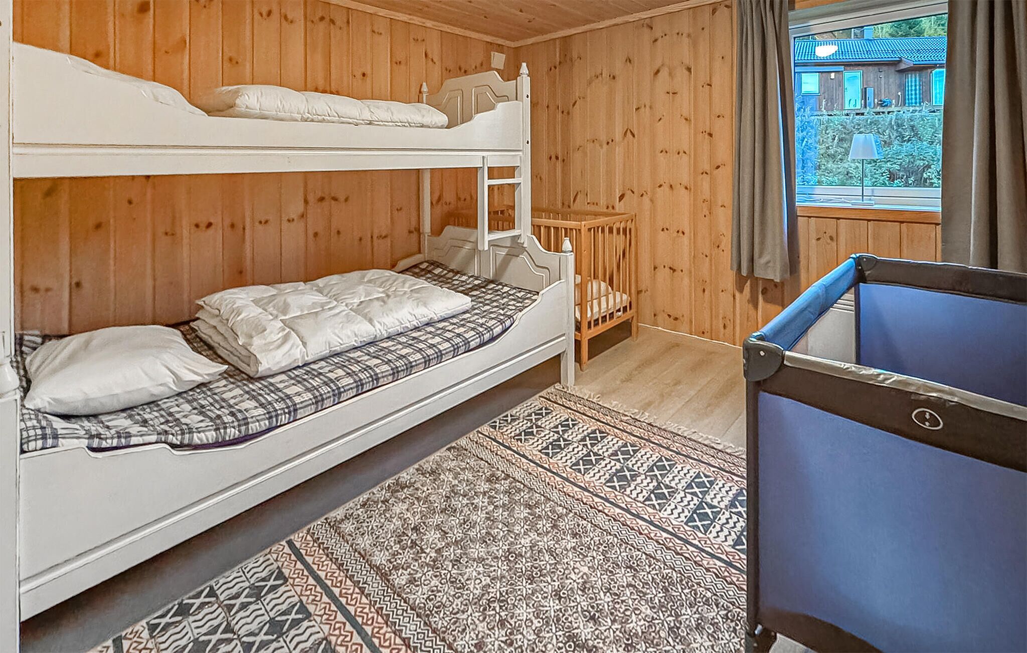 A bunk bed room with a small wooden crib, a patterned rug, and a window with curtains.