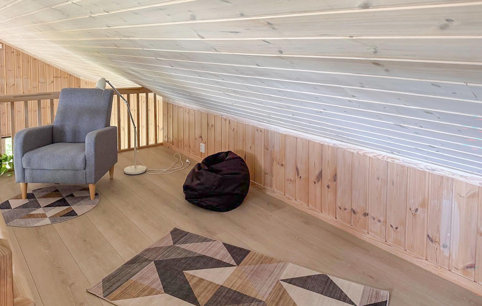 Una habitación con piso de madera, un sillón gris, un puf y una alfombra estampada.