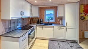 Una cucina moderna con mobili bianchi, piano cottura integrato e una finestra con vista sulle montagne.