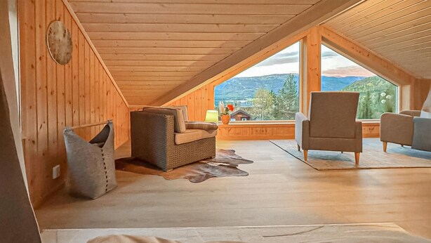 Una camera da letto mansardata accogliente, con pareti in legno e un'ampia finestra che si affaccia sulle montagne.