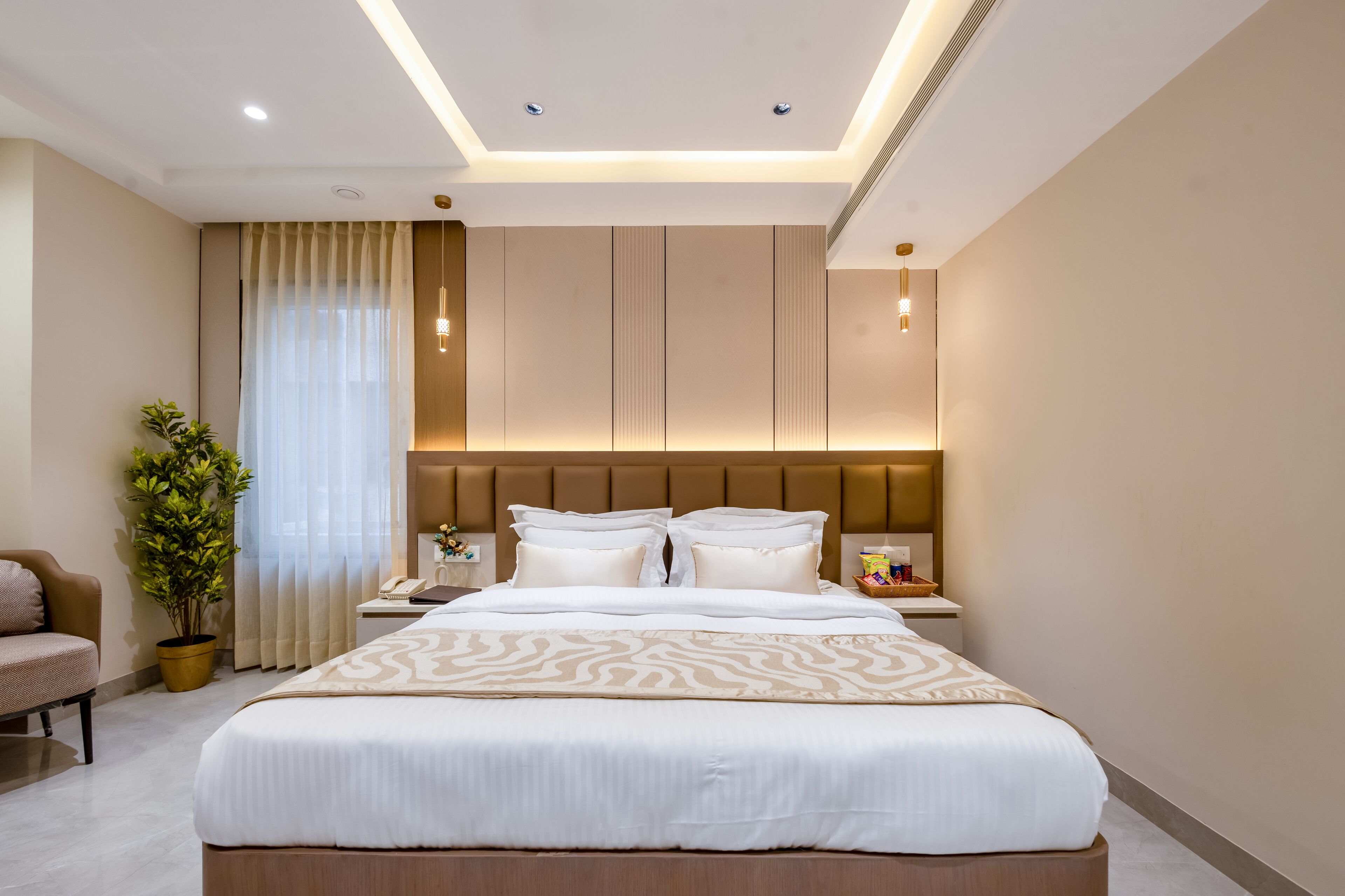 A modern hotel room with a large bed, a nightstand, a desk, a chair, and a potted plant.