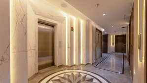 Un pasillo moderno con paredes de mármol, un diseño geométrico en el piso y líneas verticales iluminadas.