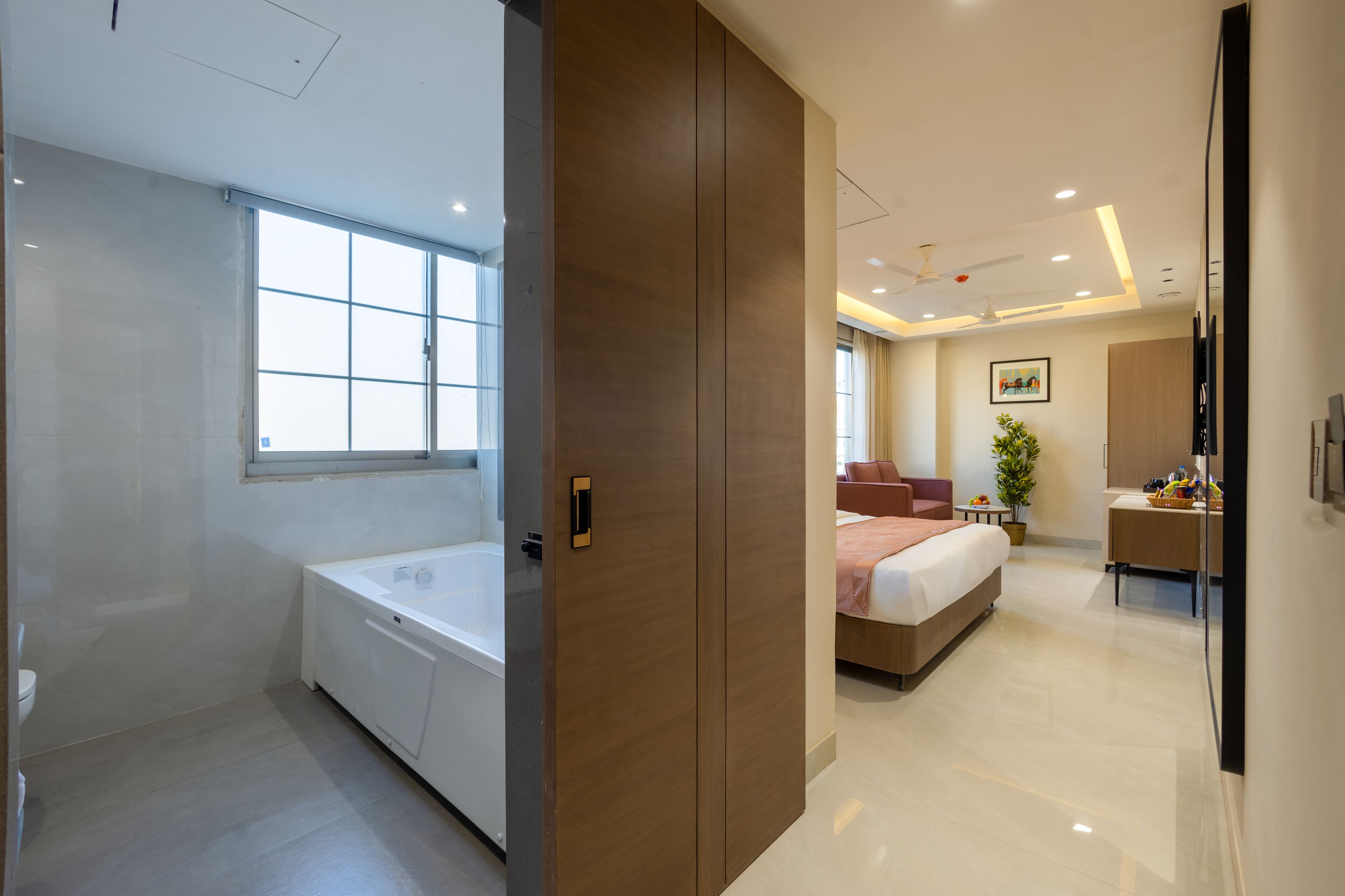 A modern hotel room with a large bed, a separate bathroom with a bathtub, a desk with a chair, and a large window providing natural light.