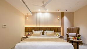 Una habitación de hotel moderna con una cama grande, una zona de estar con una silla, una mesita y un ventilador de techo.