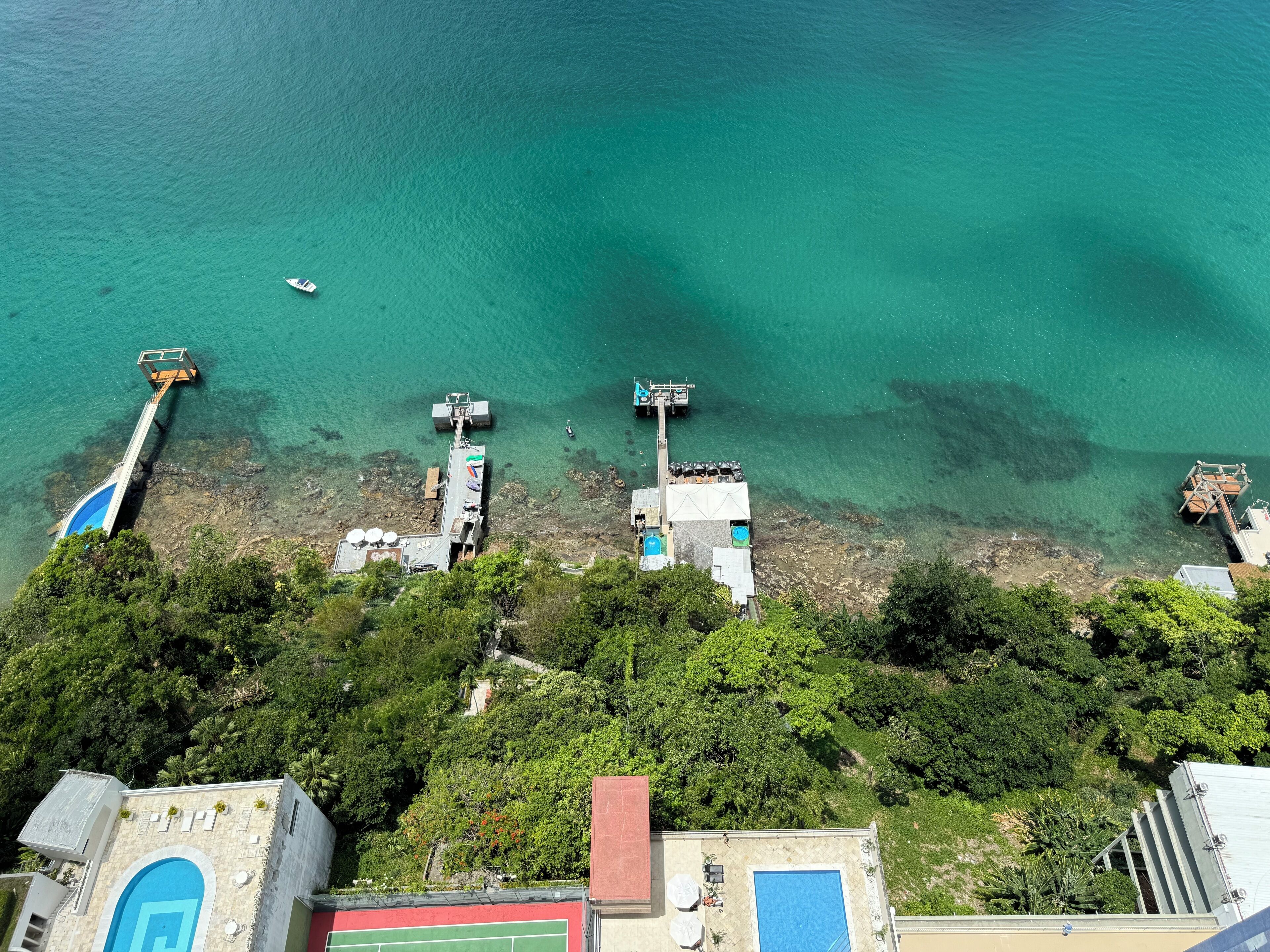 Vista aerea di una zona costiera con acque cristalline turchesi, un molo e un edificio con piscina.