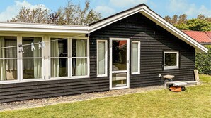 Ein schwarzes Holzhaus mit weißem Zierdekor, großen Fenstern und einer kleinen Veranda.