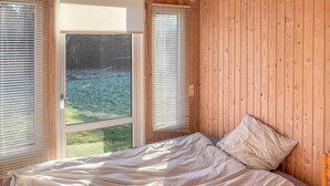 Ein Schlafzimmer mit Bett, Holzwänden und einem Fenster mit Jalousien.