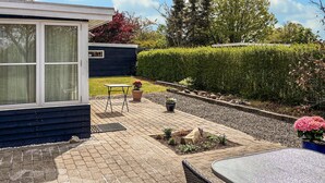 Eine Terrasse mit Tisch und Stühlen, ein kleiner Gartenbereich mit Kübelpflanzen und ein Hecke im Hintergrund.