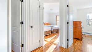Un pasillo que conduce a un dormitorio con dos camas, suelo de madera y paredes blancas.