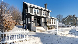 Una casa de dos pisos con un porche delantero, una chimenea y un patio cubierto de nieve.