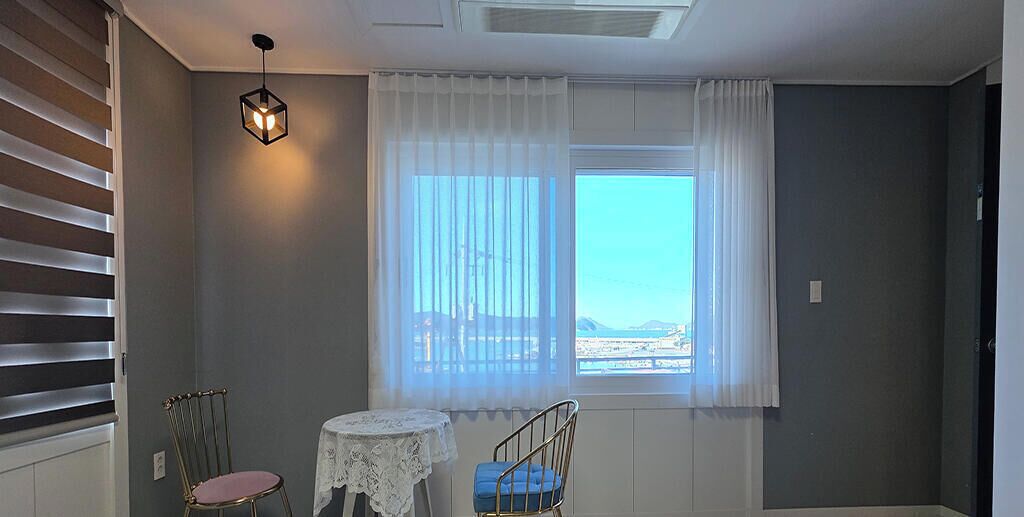 Une pièce avec une fenêtre, deux chaises, une petite table et un luminaire suspendu.
