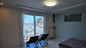 Une pièce comprenant un lit, une chaise, une petite table et offrant une vue sur le paysage urbain grâce à une grande fenêtre.