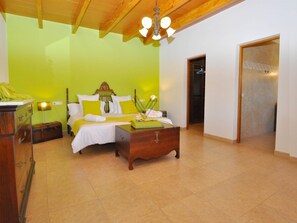 Ein Schlafzimmer mit Bett, Nachttischen, einer hölzernen Kommode und einer Tür zu einem anderen Raum.