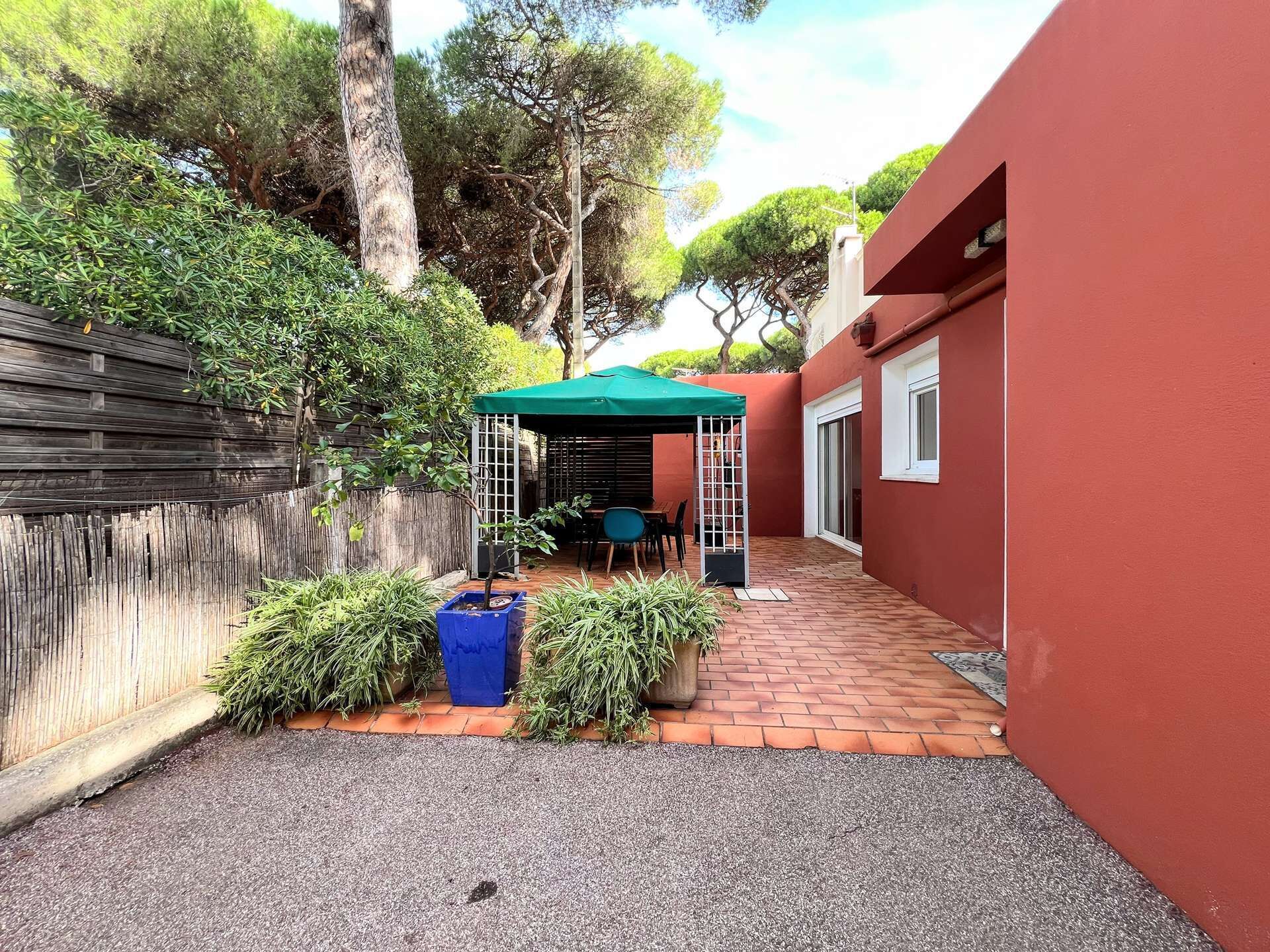 A courtyard with a covered seating area, a wooden fence, and a red wall.