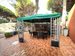 An outdoor patio with a wooden table and chairs, a green canopy, and a brick floor. - House for 6 guests with air conditioning and Wi-Fi – Hyères Port (HYERES)
