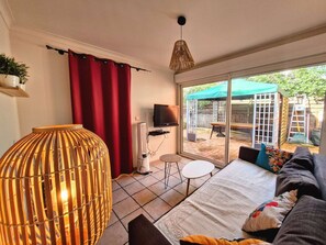 A living room with a sofa, a table, a lamp, a TV, and a sliding glass door leading to an outdoor patio. - House for 6 guests with air conditioning and Wi-Fi – Hyères Port (HYERES)
