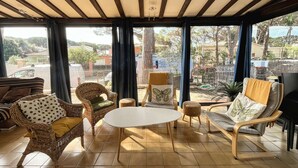 A sunlit room with a tiled floor, a round table, wicker furniture, and large windows offering a view of the outside. - House for 6 guests with air conditioning and Wi-Fi – Hyères Port (HYERES)