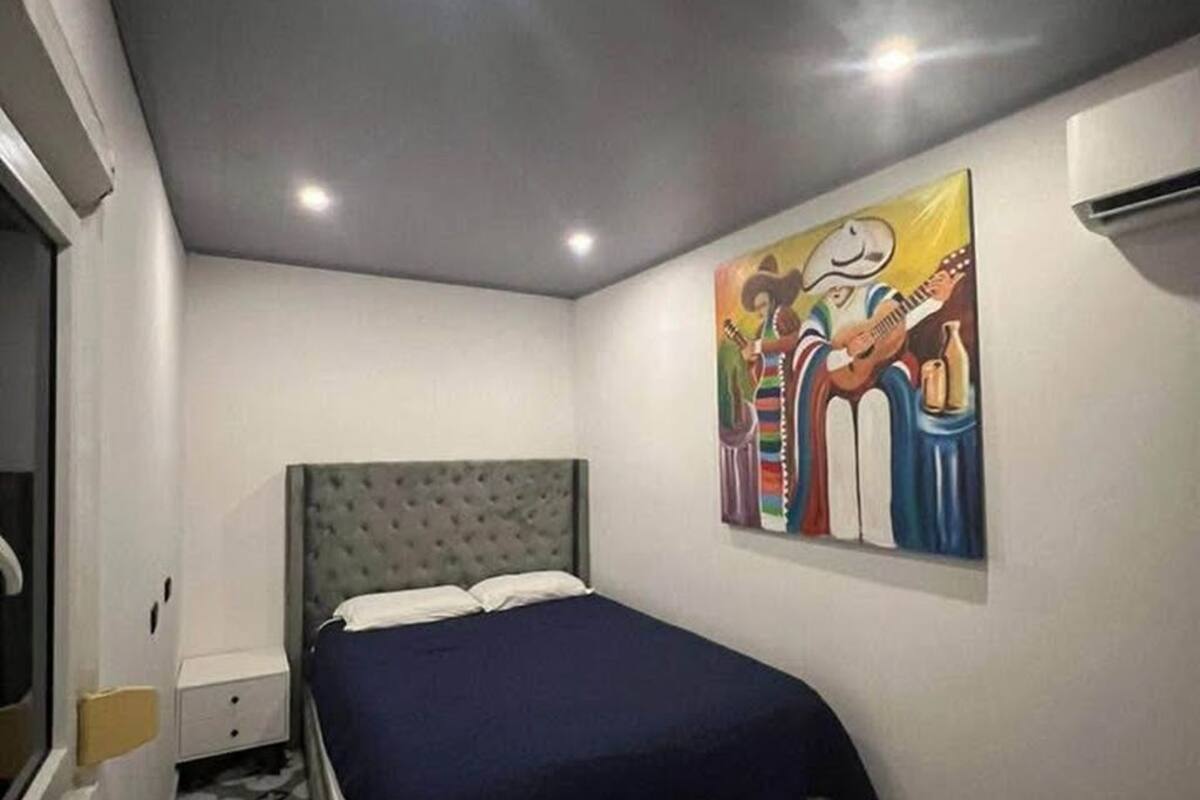 Une chambre à coucher avec un lit, une table de chevet, un climatiseur fixé au mur et un tableau coloré.