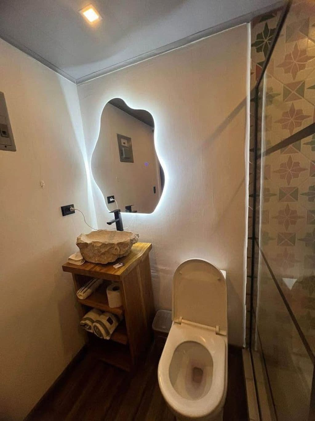 Un baño con un lavamanos original de pared, un tocador de madera y un inodoro.