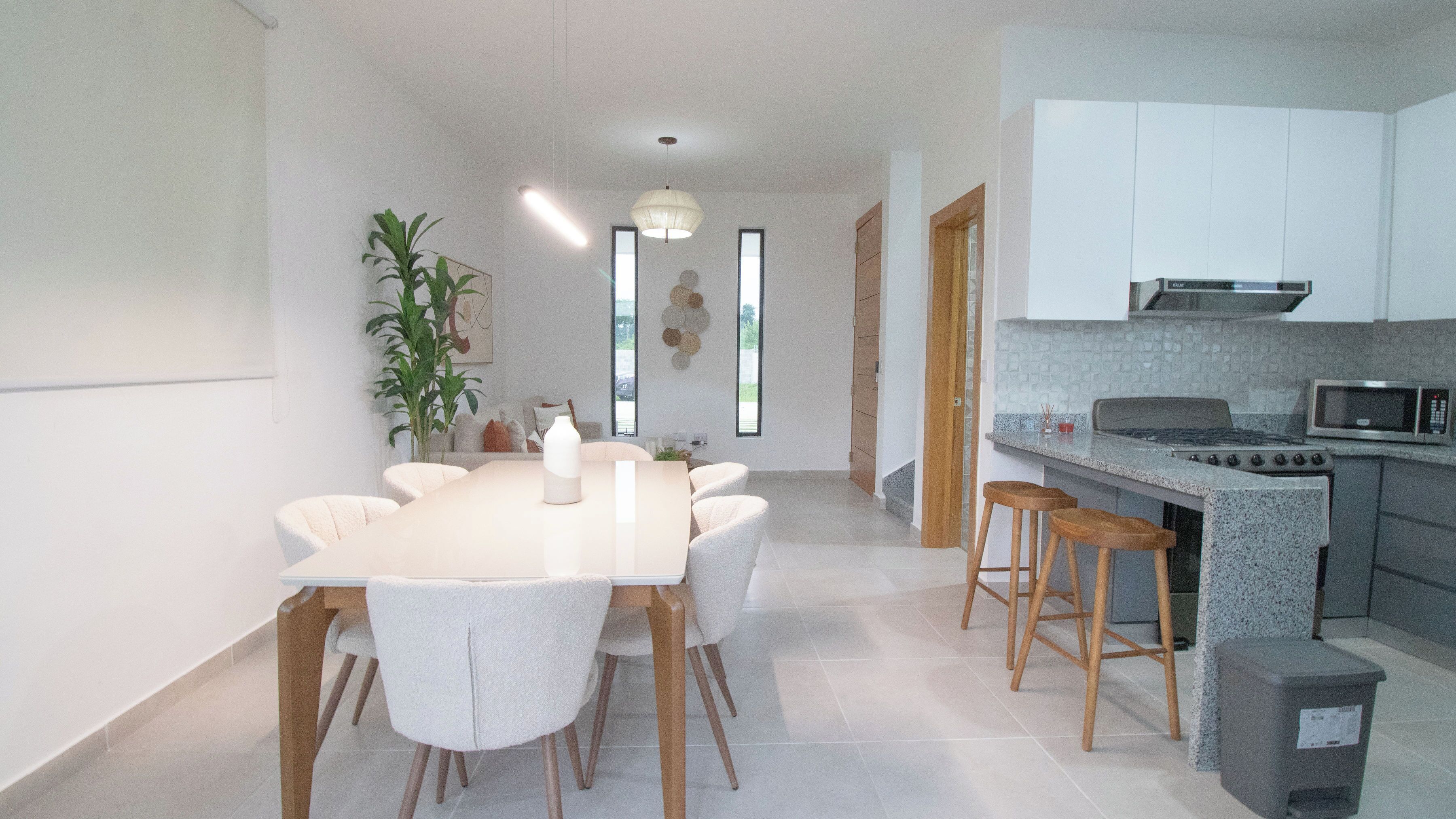 Une cuisine moderne avec des meubles blancs, un coin repas doté d’une table et de chaises blanches, et une grande fenêtre qui laisse entrer la lumière naturelle.