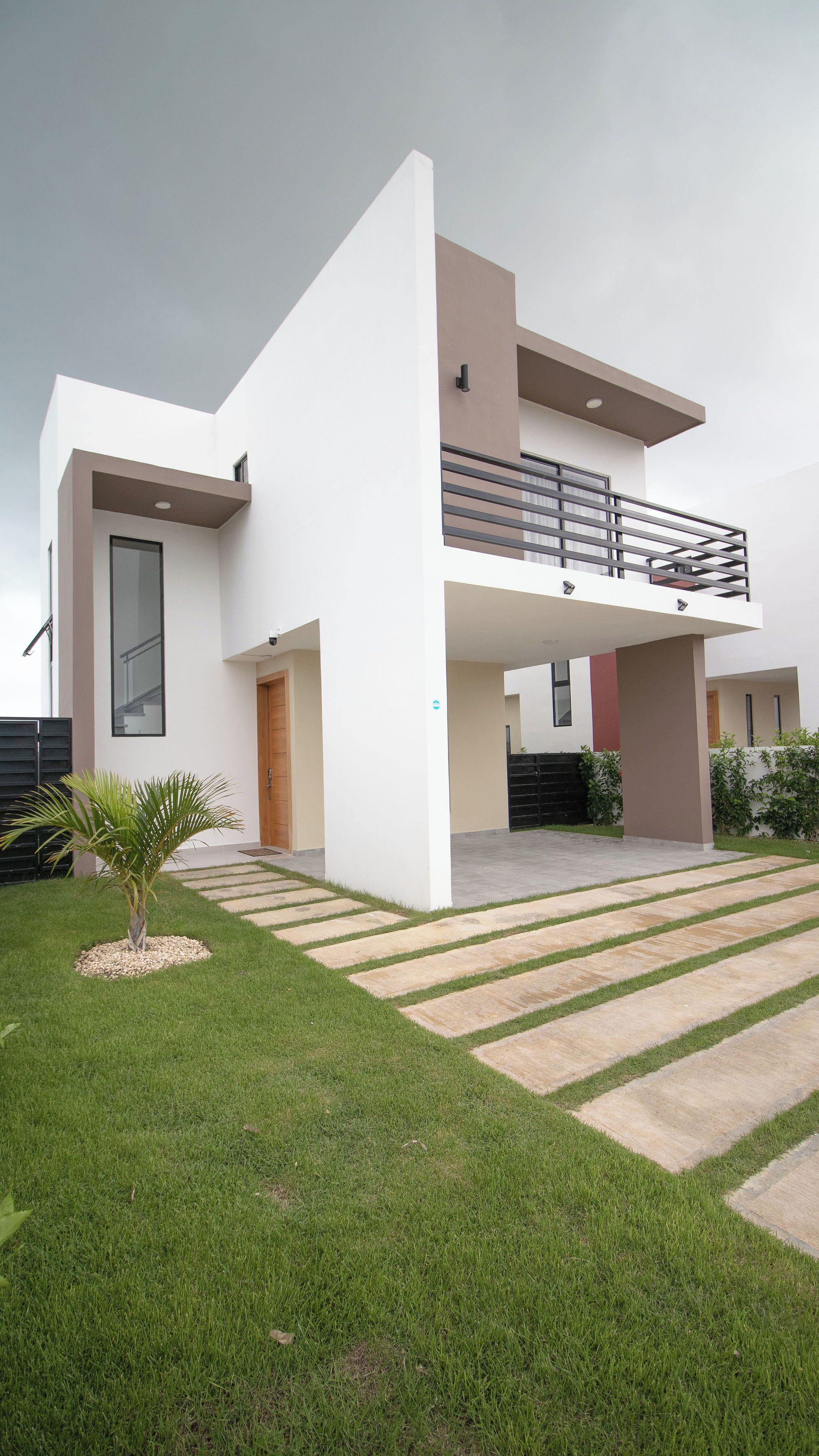 A modern two-story house with a flat roof, a balcony, and a well-maintained lawn.
