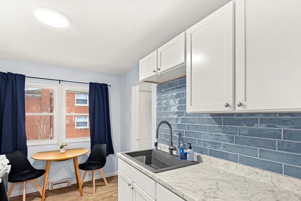 A compact kitchen with white cabinets, a sink, and a window with curtains.