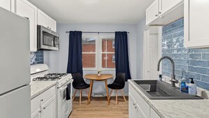A compact kitchen with white cabinets, a stove, a microwave, a sink, and a window with curtains. - Home Suite Home: E-Minutes to Downtown & P Heights (Peoria)