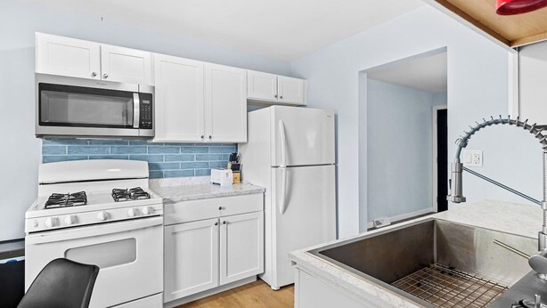 Cocina compacta con armarios blancos, microondas, estufa, refrigerador y lavaplatos con grifo moderno.