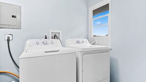 Una sala de lavandería con dos lavadoras y secadoras de carga frontal blancas, una ventana con vista al cielo y un enchufe en la pared.